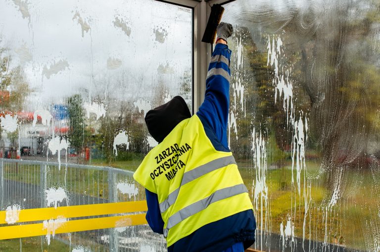 zdjęcie - Pracownik służb oczyszczania miasta myje szybę w wiacie przystankowej