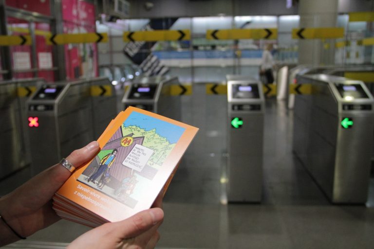 Zdjęie okładki poradnika „Savoir-vivre wobec osób z niepełnosprawnością” na tle bramek wejściowych na stację metra